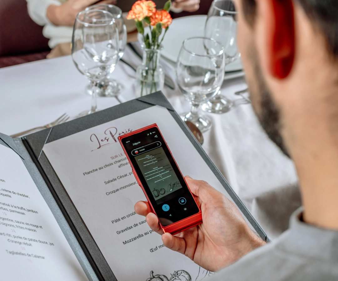 un bărbat într-un restaurant elegant care traduce meniul folosind un traducător foto dintr-un traducător electronic