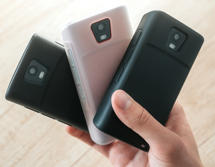 Persoană ținând în mână trei dispozitive Vasco Translator Q1 în huse din silicon, prezentând trei culori diferite: Solid Black, Dark Caramel și Milky White.