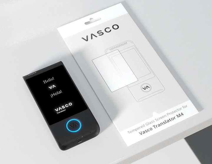 Vasco Translator M4, cu un LED albastru luminos pe butonul cu logo-ul Vasco, așezat pe o masă lângă ambalajul unei folii de protecție pentru ecran destinată modelului Vasco Translator M4.